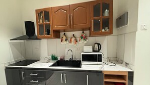 A kitchen with black cabinets, a sink, a microwave, and wooden upper cabinets with glass doors. - Mayama airport apartment (Accra)