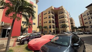 A multi-story residential building with balconies, a reception area, and parked cars. - Mayama airport apartment (Accra)