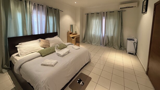 A hotel room with a large bed, a desk with a chair, an air conditioning unit, and a door. - Mayama airport apartment (Accra)