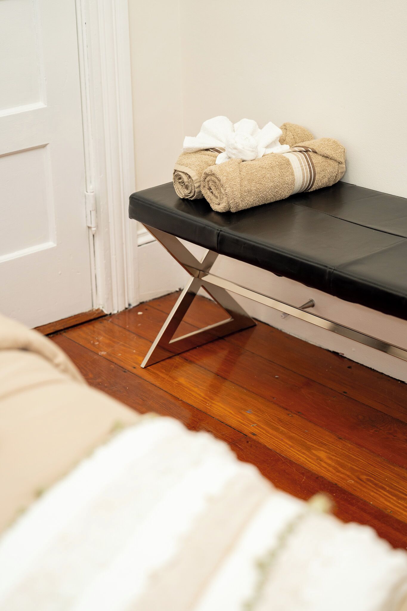 A neatly made bed with a white comforter and a rolled-up beige towel with a white bow on a black bench.