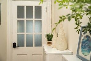 A white door with frosted glass panels, a small plant on a wooden stand, and a white textured vase on a white surface. - 8-Peaceful & Bright apt/3br right to Boston line (Milton)
