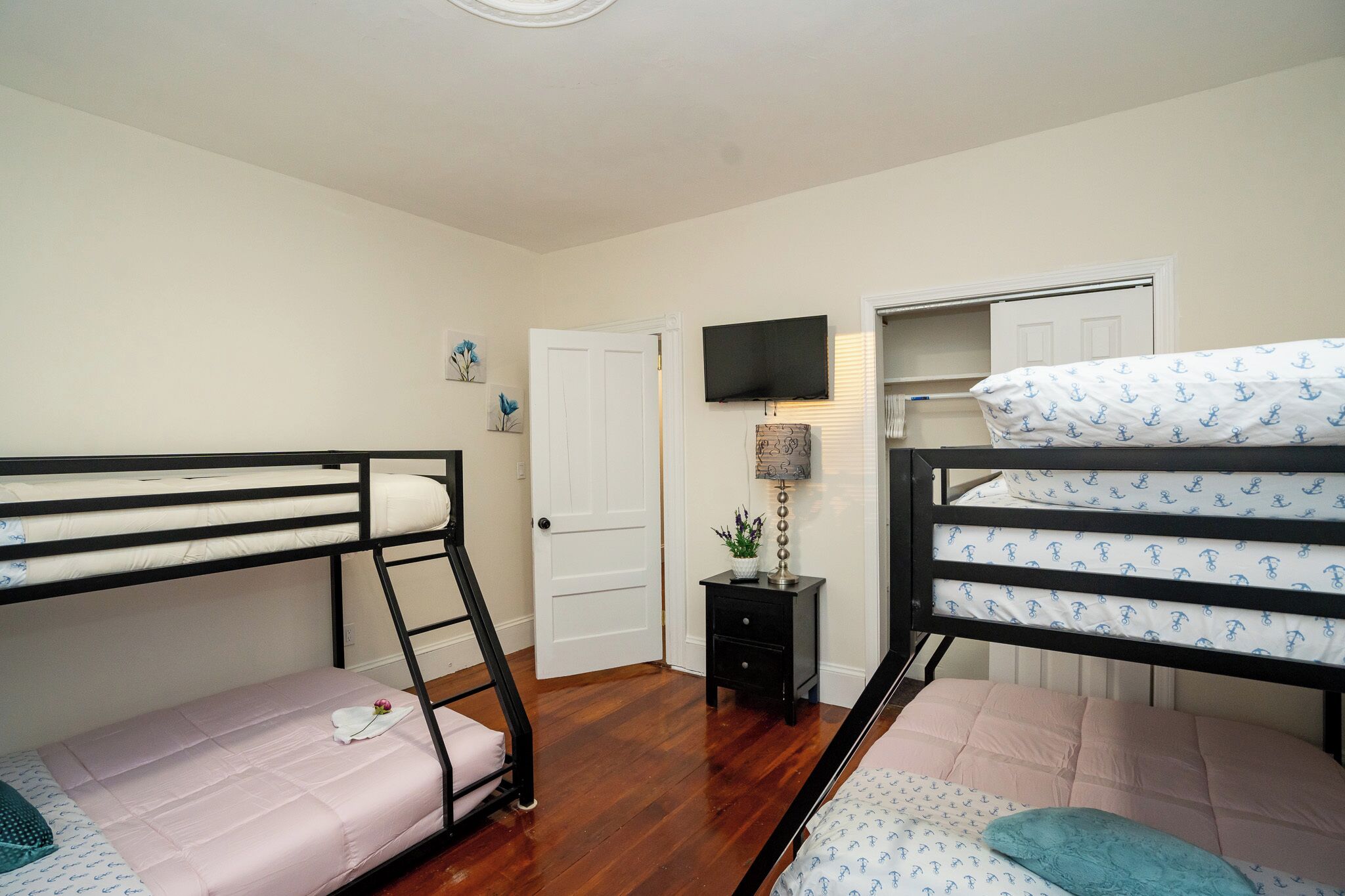 A room with two bunk beds, a television mounted on the wall, and a small bedside table with a lamp.