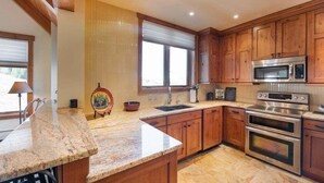 Une cuisine avec des meubles en bois, un plan de travail en granit, un four en acier inoxydable et un four à micro-ondes.