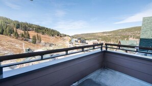 Un balcon offrant une vue sur une colline boisée et sur des bâtiments situés au loin.
