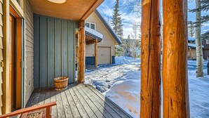 A wooden deck with a wooden bucket and a rug, leading to a house with a covered porch and a view of a snowy landscape. - 8712 Ski Tip Townhomes 3 Bedroom Townhouse (Keystone)