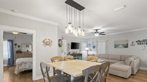A spacious living room with a wooden dining table, beige sofa, and a ceiling fan. - The Rookery Iii 4007 3 Bedroom Cottage (Gulf Shores)