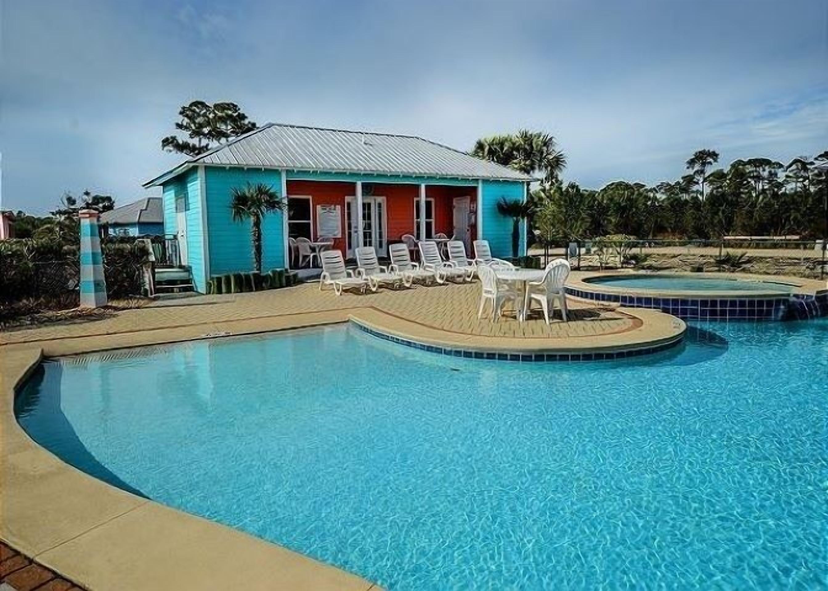 Un espace piscine avec un bâtiment aux couleurs turquoise, des chaises longues blanches et une petite piscine.