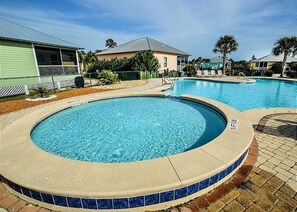 A swimming pool with a tiled edge, surrounded by a brick patio and a fence.