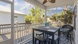 A covered outdoor area with a table and chairs, a ceiling fan, and a view of trees and a building. - The Rookery Iii 4007 3 Bedroom Cottage (Gulf Shores)