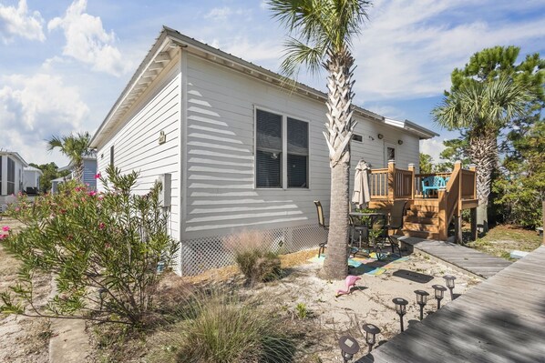 A single-story white house with a wooden deck, a small porch, and a palm tree.