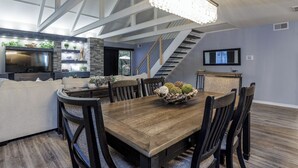 A modern dining area with a wooden table and chairs, a chandelier, and a staircase leading to an upper level.