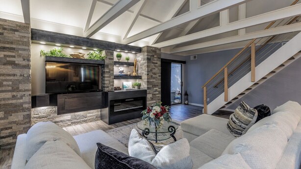 A modern living room with a fireplace, a large TV, and a staircase leading to another level.