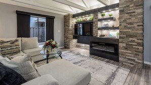A modern living room with a stone accent wall, a flat-screen TV, and a fireplace.