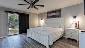 A bedroom with a large bed, a ceiling fan, a sliding glass door to a balcony, and a wall-mounted sign.