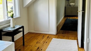 A room with wooden flooring, a white door, a small table with a vase, and a view of a garden through a window.