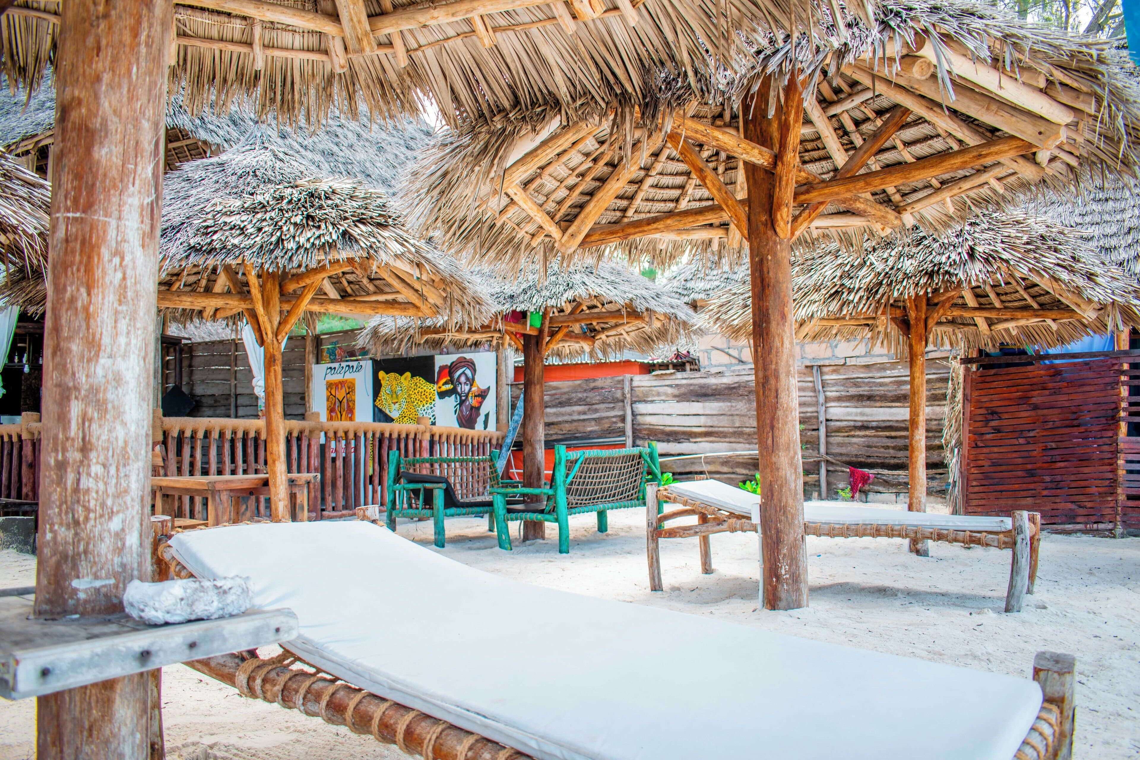 A beachside hut with thatched roofs, wooden benches, and a small table.
