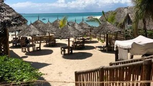 Un complexe hôtelier en bord de mer, doté de parasols à toit de chaume, de tables et de chaises en bois.