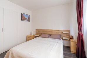A bedroom with a bed, wooden headboard, bedside tables, a nightstand, a lamp, a picture on the wall, and a curtain. - Bright & Contemporary 2BD Apartment (Paris)
