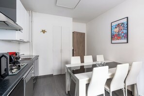 A modern kitchen with a gas stove, a coffee machine, and a dining area with a glass table and white chairs. - Bright & Contemporary 2BD Apartment (Paris)