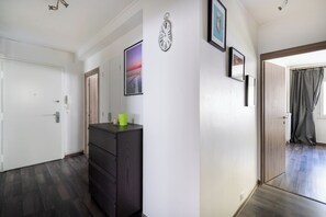 A hallway with a wooden door, a dark-colored dresser with a green object on top, and a framed clock on the wall. - Bright & Contemporary 2BD Apartment (Paris)