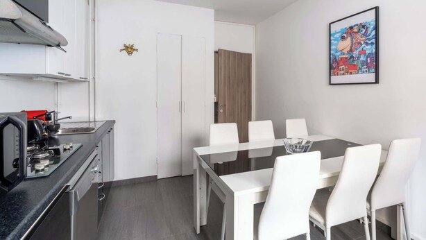 A modern kitchen with a gas stove, white cabinets, and a dining area with a glass table and white chairs. - Bright & Contemporary 2BD Apartment (Paris)