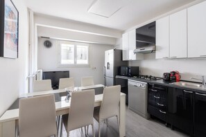 A modern kitchen with a dining area, equipped with a refrigerator, stove, microwave, and dishwasher. - Bright & Contemporary 2BD Apartment (Paris)