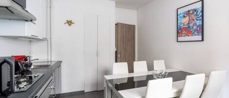 A modern kitchen with a gas stove, a coffee machine, and a dining area with a glass table and white chairs.