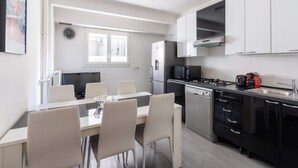 A modern kitchen with white cabinets, a dining table with chairs, a clock, and a window. - Bright & Contemporary 2BD Apartment (Paris)