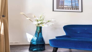 A blue sofa and a blue vase with white flowers. - Bright & Contemporary 2BD Apartment (Paris)