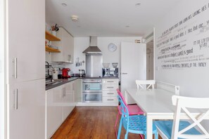 Una cocina moderna con armarios blancos, electrodomésticos de acero inoxidable y un comedor con una mesa blanca y sillas coloridas.