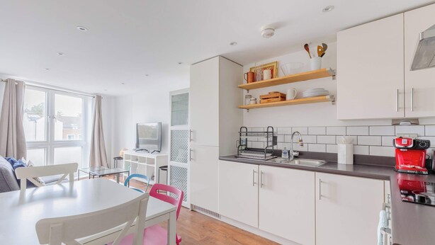 A modern kitchen with white cabinets, a dining table with chairs, a coffee machine, and a TV.