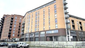 A multi-story building with a curved facade, balconies, and a parking area in front.