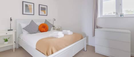 Un dormitorio moderno con una cama, mesitas de noche, un radiador y una ventana.
