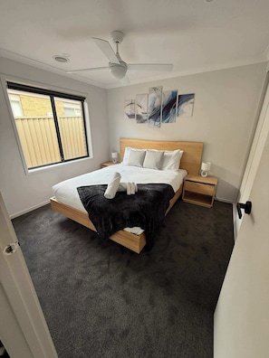 Una camera da letto con un letto, una ventola a soffitto, una finestra, opere d'arte alle pareti e un comodino con una lampada.