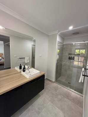 Un bagno moderno con un mobile bagno in legno, uno specchio grande, cabina doccia in vetro e un portasciugamani a vista.