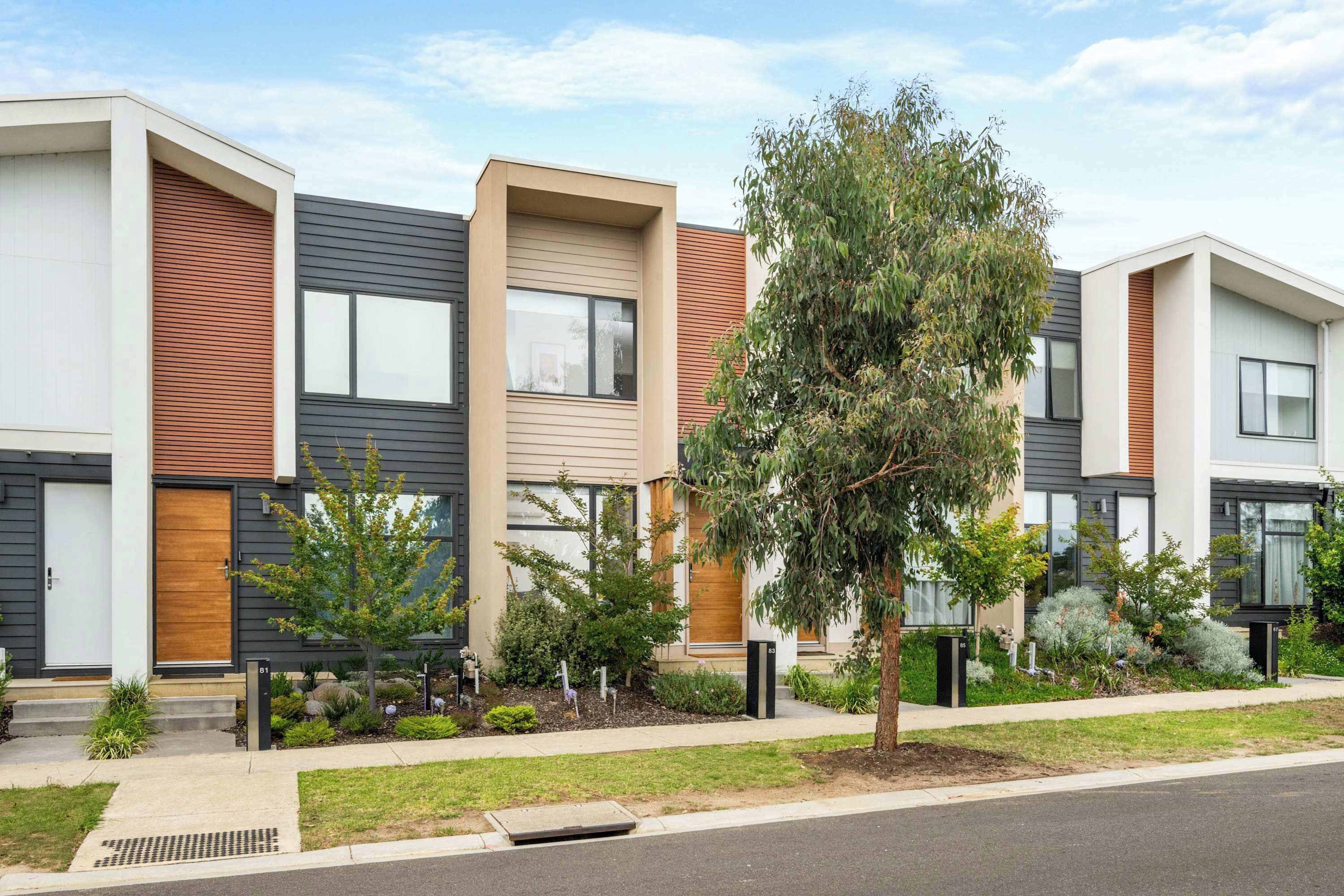 A row of modern townhouses with a central garden, a driveway, and a clear sky.