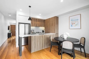 A modern kitchen with a central island, a dining area with two chairs, and a framed artwork on the wall. - Beautiful 2BR on Bright, Torquay (Torquay)