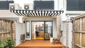 Una casa moderna con terraza de madera, puerta corrediza de vidrio que da a una cocina y un pequeño jardín.