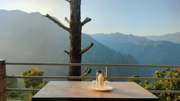 Una mesa con una botella y vasos, un árbol y vistas de montañas.