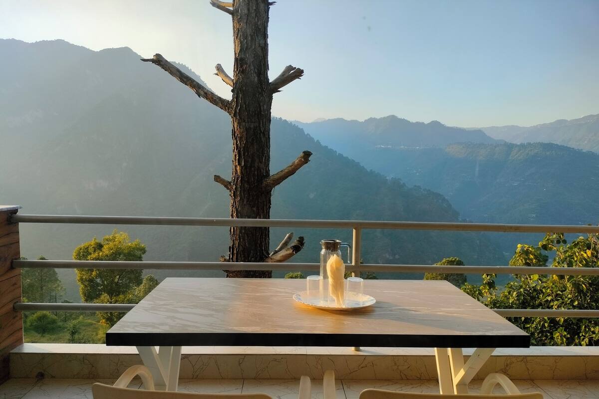 A table with a bottle and glasses, a tree, and a view of mountains.