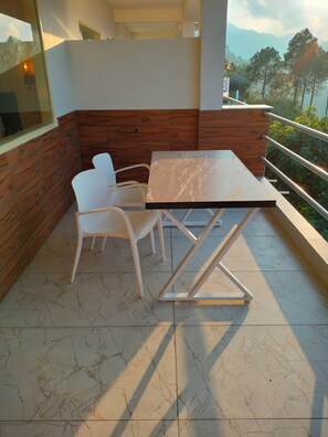 A modern outdoor seating area with a table and chairs, wooden paneling on the walls, and a view of the mountains in the background. - SVS RECREATIONAL HOTELS AND RESORTS (Tehri)