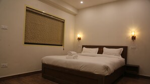 Una cama bien hecha con sábanas y almohadas blancas, un cabecero de madera y dos lámparas fijadas a la pared.
