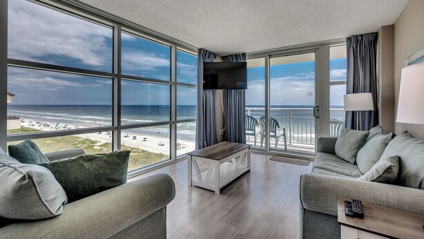 A modern hotel room with a large balcony, a sofa, a coffee table, and a TV. - 🐠🌞Oceanfront | Corner Unit | Resort Amenities | Seaside Resort 603 (North Myrtle Beach)