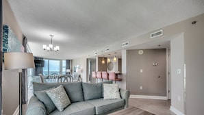 A modern living room with a grey sofa, a wooden coffee table, and a dining area in the background. - 🐠🌞Oceanfront | Corner Unit | Resort Amenities | Seaside Resort 603 (North Myrtle Beach)