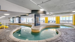 An indoor swimming pool with a curved design, surrounded by tiled walkways and yellow pillars. - 🐠🌞Oceanfront | Corner Unit | Resort Amenities | Seaside Resort 603 (North Myrtle Beach)