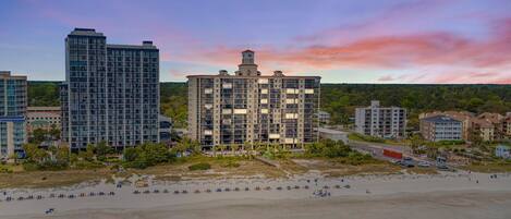 Et hotel ved stranden med flere høje bygninger, en sandstrand og en klar himmel.