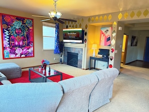 A living room with a fireplace, a television, a sofa, and a colorful abstract painting. - GolfSim HotTub PS5 Sauna Thtr Pooltbl 6BR 5BA 420 (Thornton, CO, 80602)