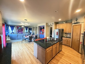 A modern kitchen with wooden cabinets, a stainless steel refrigerator, and a dining area with a table and chairs. - GolfSim HotTub PS5 Sauna Thtr Pooltbl 6BR 5BA 420 (Thornton, CO, 80602)