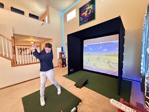 A person playing golf indoors with a large screen displaying a golf course. - GolfSim HotTub PS5 Sauna Thtr Pooltbl 6BR 5BA 420 (Thornton, CO, 80602)