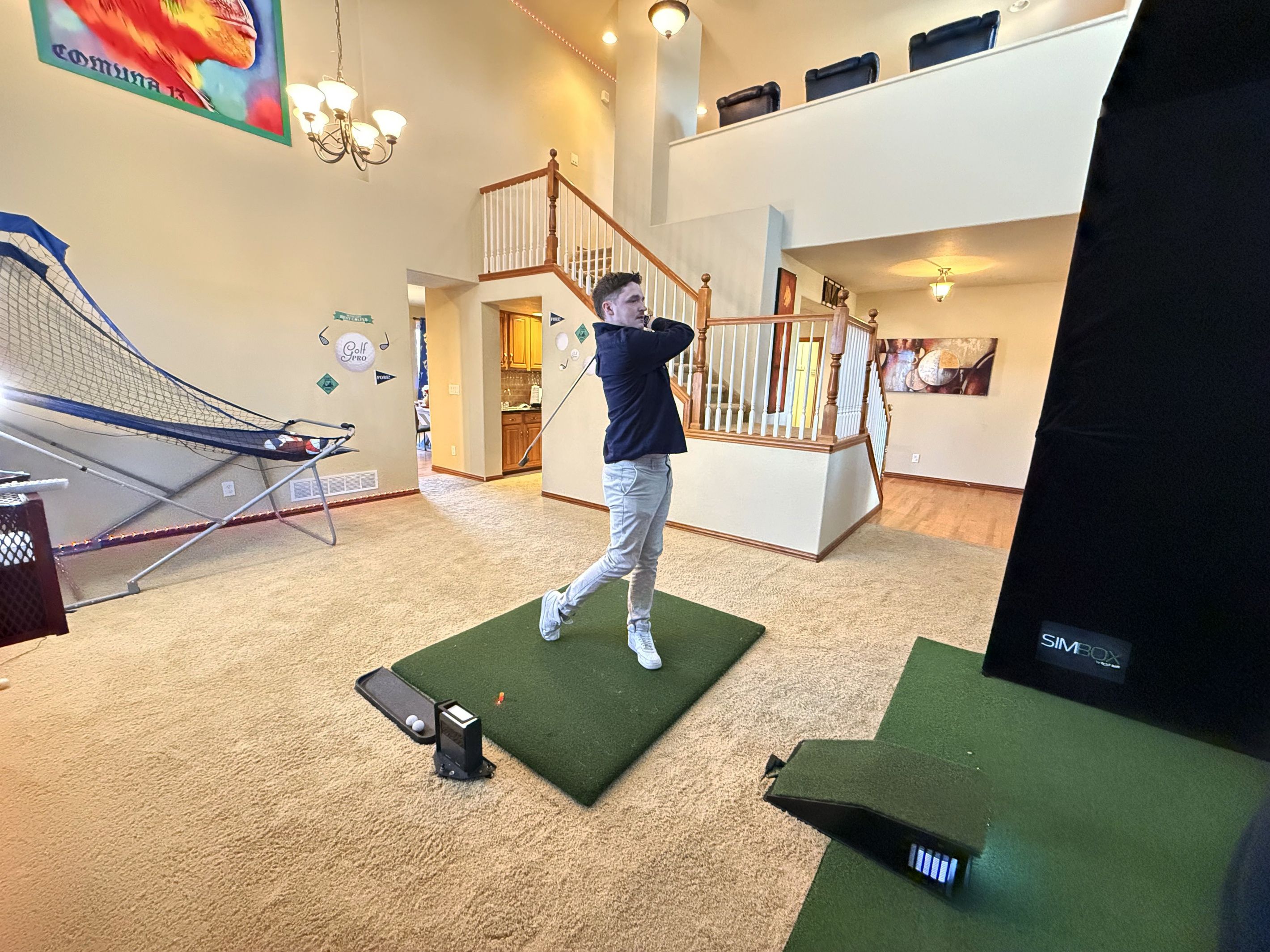 A person practicing golf indoors with a netted area and a staircase.